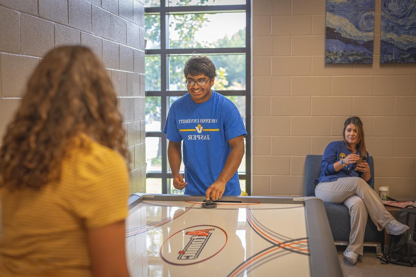 Two students playing air hockey while another watches