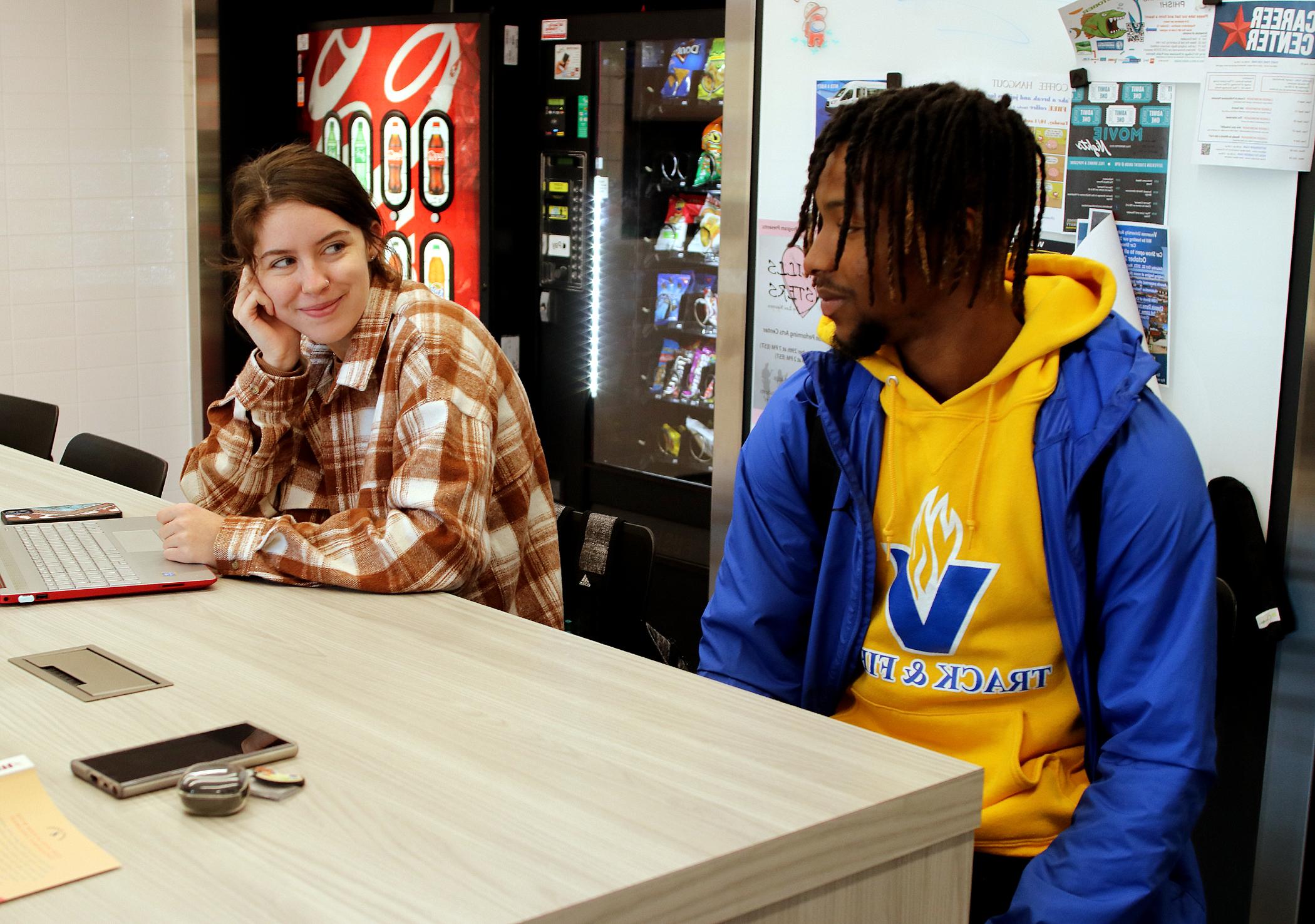 Two students sitting at a table in front of some vending machines