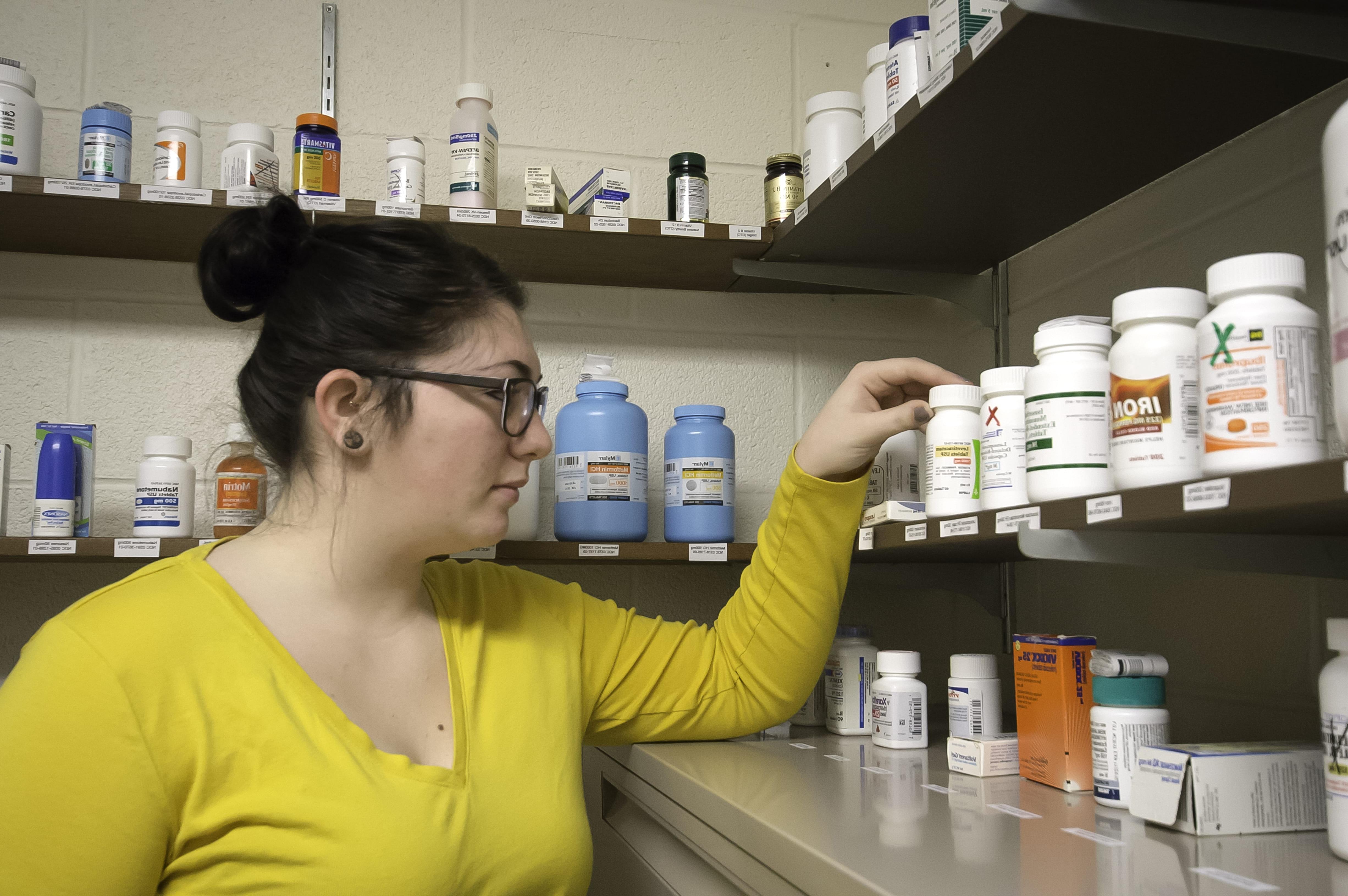 A pharmacy student grabbing a pill bottle from the shelf