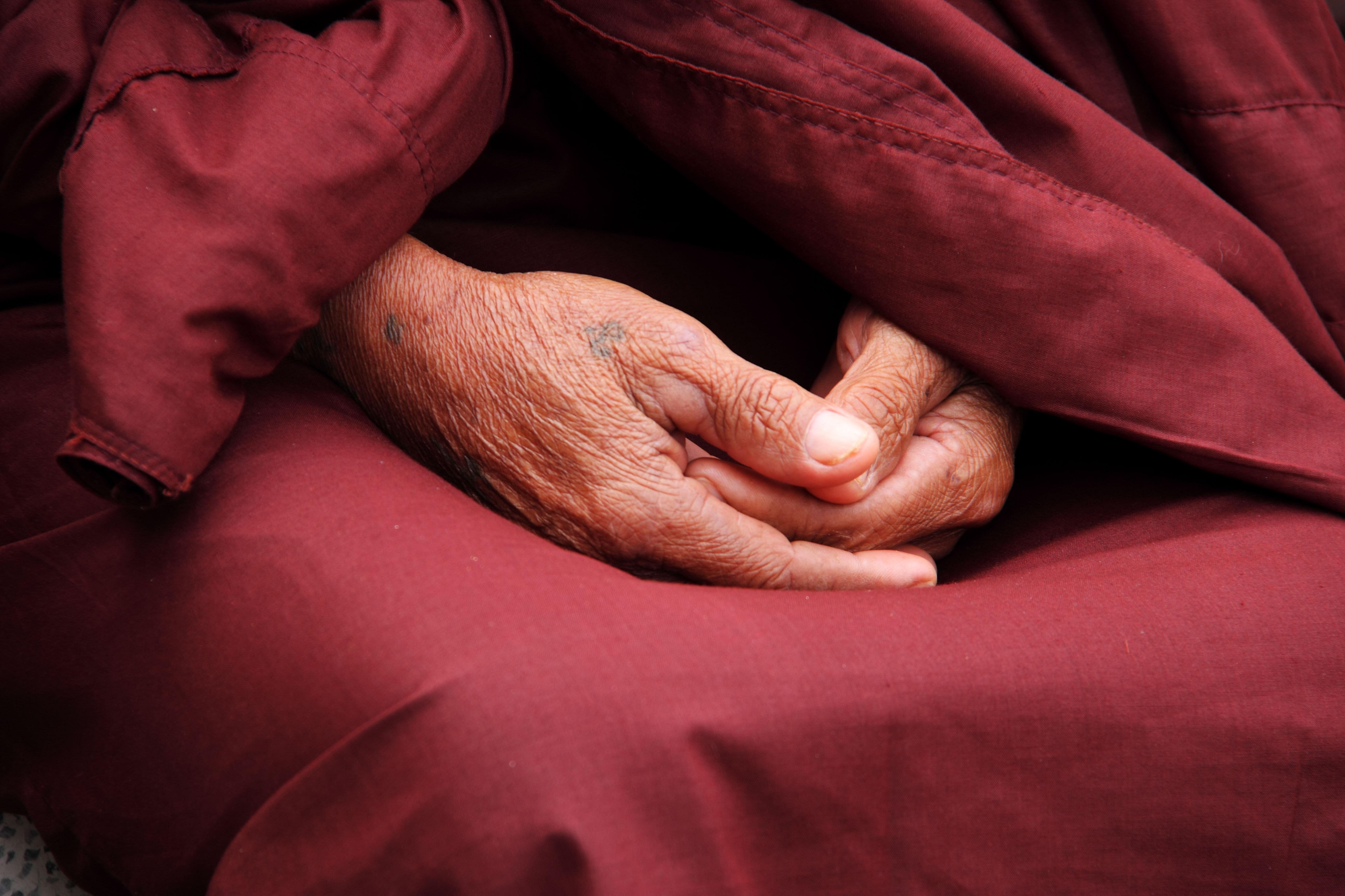 Monk folding their hands in their lap with a maroon robe