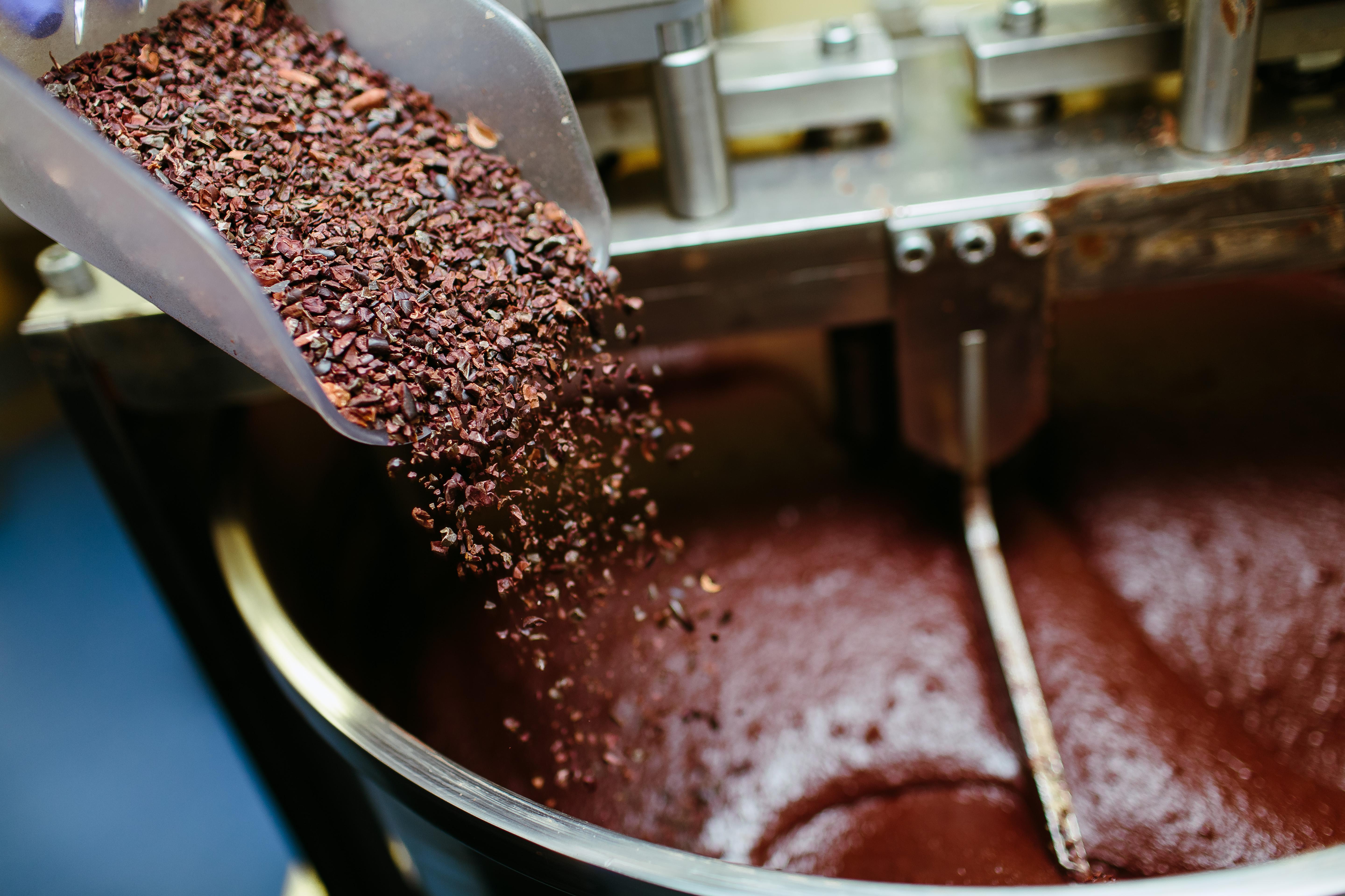 Cocoa grits being poured into a grinder full of chocolate.